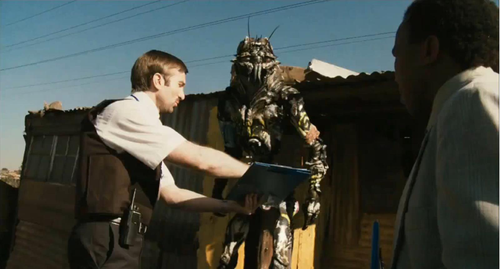 district-9 Wikus (Sharlto Copley) explains to one of the aliens that it's time to go.